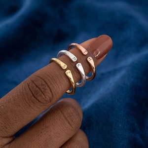 May include: Three open-ended rings in gold, silver, and rose gold tones. Each ring features a single stamped letter on the end. The gold ring is stamped with S and Z, the silver ring with M and K, and the rose gold ring with T and H.