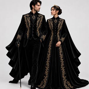 May include: Two people in matching black velvet outfits with gold embroidery. One wears a suit with a cape and holds a cane. The other wears a long dress with a cape and a gold crown. The outfits have ornate gold floral patterns.