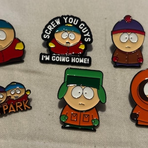 May include: A selection of enamel pins featuring characters from the animated series South Park. The pins depict Cartman, Stan, Kyle, Kenny, and other characters. One pin reads "Screw You Guys I'm Going Home!"