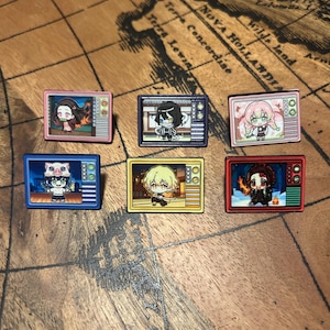 May include: A set of six rectangular enamel pins shaped like vintage television sets, each displaying a different chibi-style anime character. The pins feature vibrant frames in pink, dark blue, light pink, blue, yellow, and red, with detailed screen graphics.