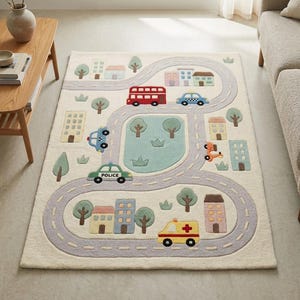 May include: A rectangular area rug with an off-white background featuring a light gray road pattern, colorful buildings, green trees, and various vehicles including a red double-decker bus, a police car, and an ambulance with a red cross symbol.