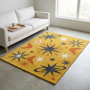 Peut inclure: Tapis jaune moutarde au design moderne du milieu du siècle. Le tapis présente des formes d'éclats d'étoiles et de boomerangs bleu marine, blancs et orange. Le tapis rectangulaire est posé sur un sol en béton.