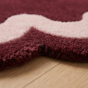 May include: A tufted rug featuring a thick, plush pile with a wavy, organic pattern. The design consists of deep burgundy and soft light pink sections that create a bold, contrasting color block effect across the textured surface of the rug.