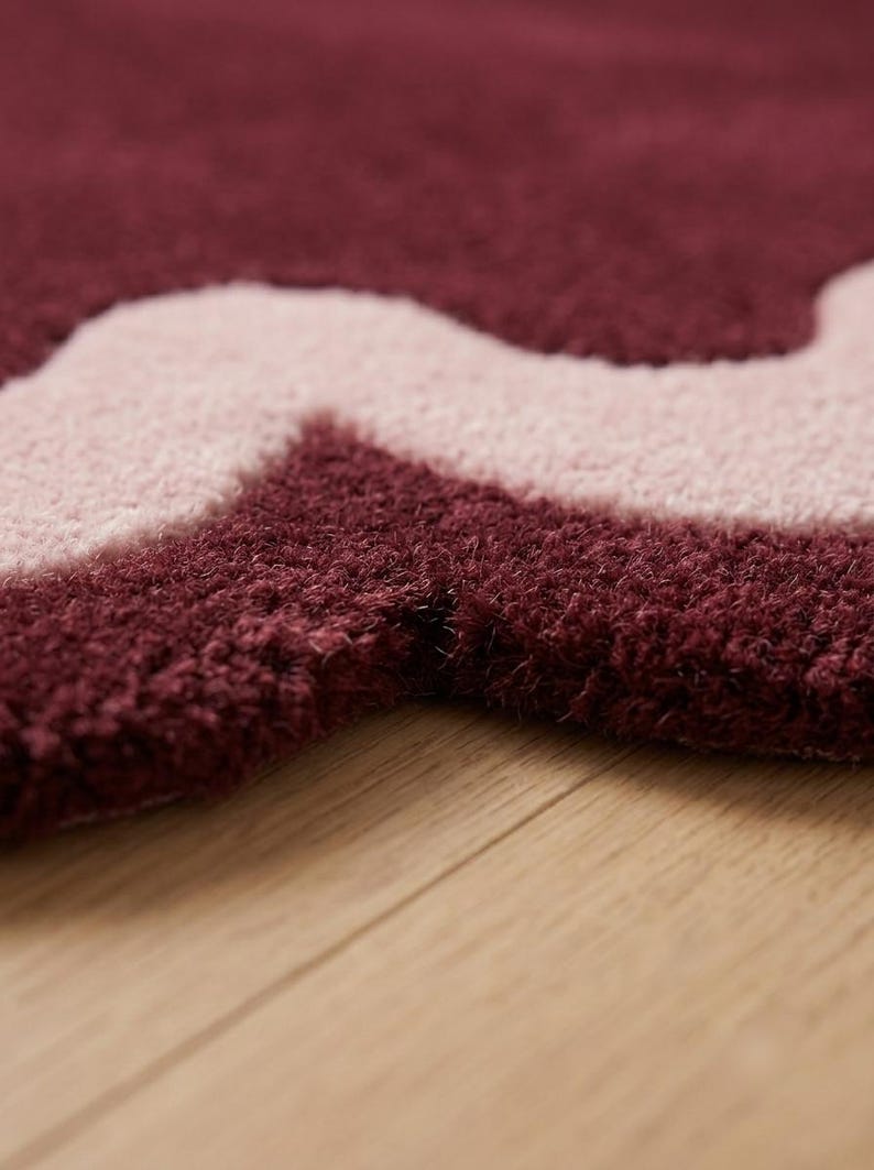 May include: A tufted rug featuring a thick, plush pile with a wavy, organic pattern. The design consists of deep burgundy and soft light pink sections that create a bold, contrasting color block effect across the textured surface of the rug.