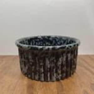 May include: A round ceramic bowl featuring a dark black base color with a white speckled, drip-like glaze pattern covering the exterior and the inner rim. The bowl has a distinct vertical ribbed texture along its outer wall and a smooth, wide opening.