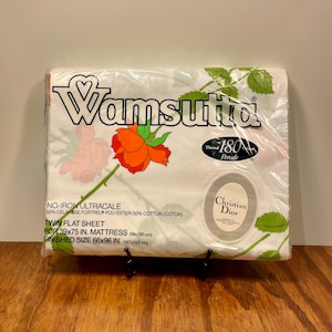 May include: A packaged Wamsutta twin flat sheet featuring a floral rose pattern in orange and red on a white background. The packaging includes the Christian Dior logo and details about the 180 thread count percale sheet, sized for a 39x75 inch mattress.