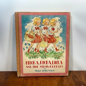 May include: A hardback book titled Flicka, Ricka, Dicka and the Strawberries by Maj Lindman. The cover features an illustration of three blonde children in white shirts and red skirts carrying baskets in a field with blue flowers and strawberries.