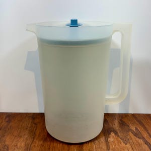 May include: A translucent plastic pitcher with a handle and a lid. The pitcher is a light, off-white color with a blue lid and handle. The pitcher is approximately 9 inches tall.