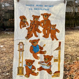 May include: A vintage kitchen towel with brown bear illustrations. The text "INVITE MORE BEARS TO BREAKFAST" is printed at the top. Bears are depicted in various poses, some wearing aprons and bow ties. The towel is hanging on a clothesline.