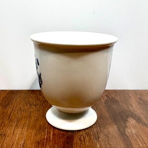 Puede incluir: Copa de cer&aacute;mica color crema con borde y base blancos. La copa presenta un dise&ntilde;o floral azul oscuro y una base de pedestal. La copa est&aacute; sobre una superficie de madera.
