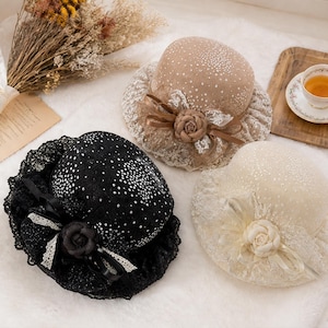 Puede incluir: Tres sombreros en negro, beige y crema, cada uno con una copa redondeada, un ala ancha con ribete de encaje, una rosa de tela decorativa y una dispersión de pequeñas lentejuelas plateadas reflectantes sobre la superficie del sombrero.