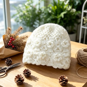 May include: A white crochet beanie featuring a textured floral pattern throughout the knit. The hat is crafted from soft yarn with a scalloped edge, showcasing intricate flower motifs that cover the entire surface of the headwear.