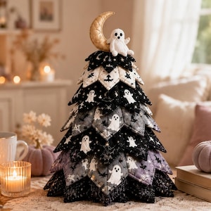 May include: A decorative fabric tree featuring layered, quilted triangular panels in black, gray, and white. The fabric displays patterns of ghosts, bats, and spiderwebs. A gold crescent moon and a small white plush ghost sit at the top.