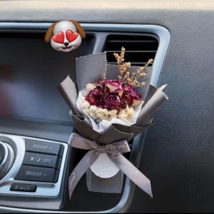 Könnte beinhalten: Ein kleiner Strauß aus getrockneten dunkelroten Rosen und weißen Füllblumen, eingewickelt in dunkelgraues Papier. Ein graues Schleifenband trägt den weißen Aufdruck for you. Ein Hundeaufkleber mit Herzaugen ist über dem Strauß angebracht.