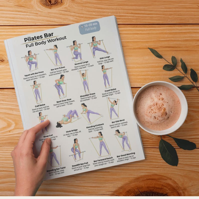 May include: A Pilates Bar Full Body Workout guide with illustrated exercise instructions. The guide is on a white paper with a wooden background. A cup of coffee and a sprig of leaves are next to the guide.