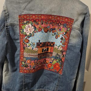 Peut inclure: Veste en jean bleu clair avec un patch coloré à motifs floraux dans le dos. Le patch présente une illustration détaillée d'une calèche, entourée de fleurs et de feuillages. La veste a un col classique et une fermeture boutonnée.