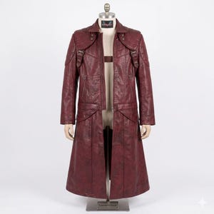 May include: A burgundy leather coat with a long, flowing design. The coat features a notched collar, shoulder epaulets, and multiple pockets. The coat is displayed on a mannequin. The words "Limited Edition" are visible on the base.