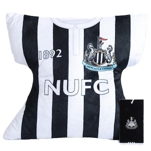 May include: A plush pillow shaped like a Newcastle United football jersey. The pillow features black and white stripes, the number "1892", and the letters "NUFC". The team crest is displayed on the upper right. A black tag with the team crest is attached.