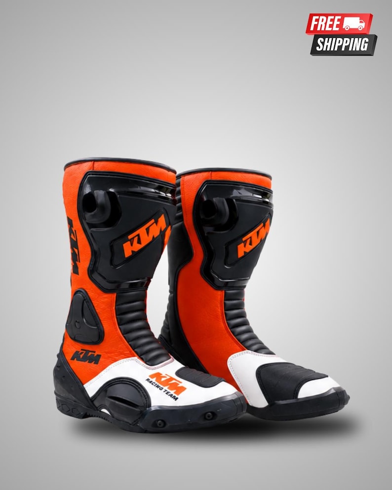 May include: A pair of motorcycle boots in bright orange, black, and white. The boots feature the KTM logo in orange on the black shin guard and the text KTM RACING TEAM on the white toe section. They include black accordion panels and protective gear.