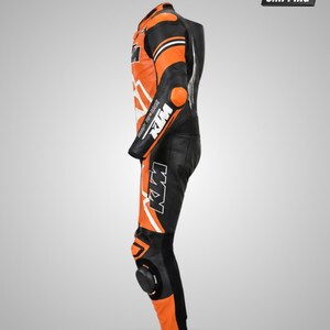 May include: A black and orange motorcycle racing suit featuring the KTM logo on the chest, arm, and leg. The suit includes protective padding on the shoulder, elbow, and knee areas, with white accents and branding text visible along the side profile.