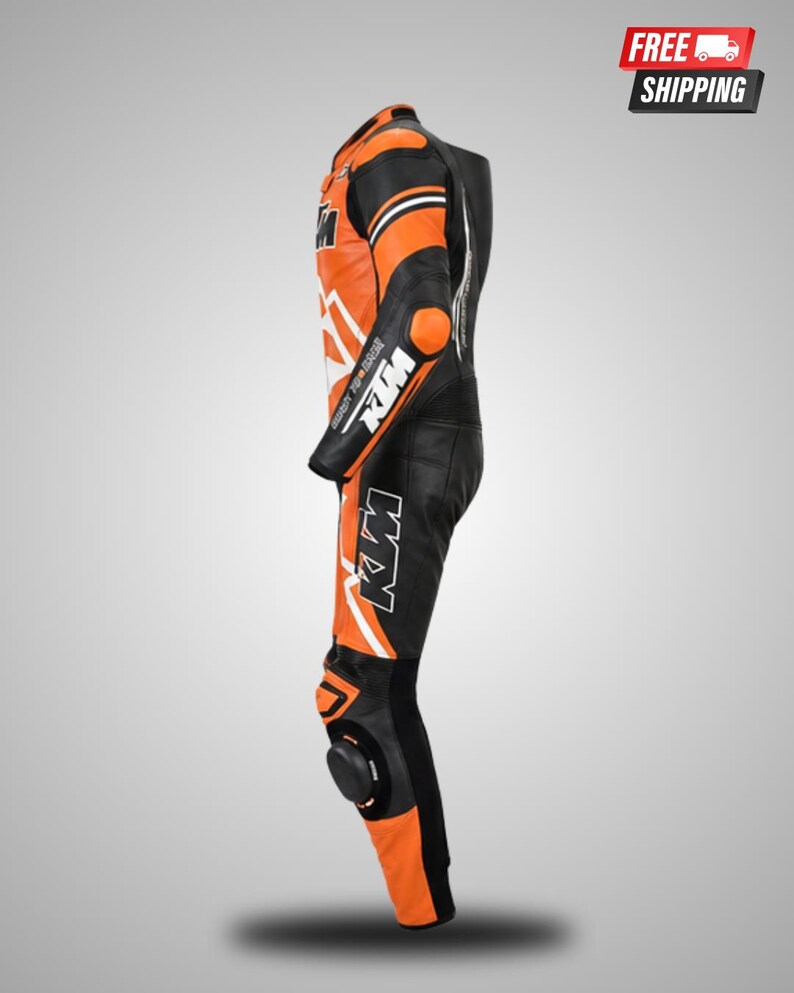 May include: A black and orange motorcycle racing suit featuring the KTM logo on the chest, arm, and leg. The suit includes protective padding on the shoulder, elbow, and knee areas, with white accents and branding text visible along the side profile.