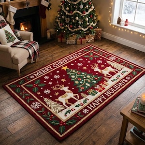 Op de afbeelding: Een rechthoekig vloerkleed met een dieprode achtergrond, een centrale kerstboom, twee witte rendieren en cadeautjes. De rand toont hulstbladeren, bessen en sneeuwvlokken, met de tekst MERRY CHRISTMAS en HAPPY HOLIDAYS.
