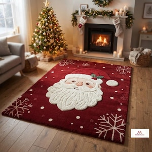 Op de afbeelding: Een rechthoekig vloerkleed in donkerrood met een groot, gecentreerd, getextureerd wit gezicht van de Kerstman met een rode muts, geaccentueerd door witte sneeuwvlokpatronen en kleine witte stippen verspreid over het oppervlak.