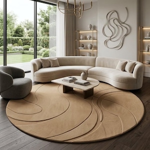 May include: A large round beige area rug with a textured, swirling wave pattern placed on a dark wood floor. The rug features a low-pile surface with carved lines that create a sense of movement, centered beneath a curved sofa and coffee table.
