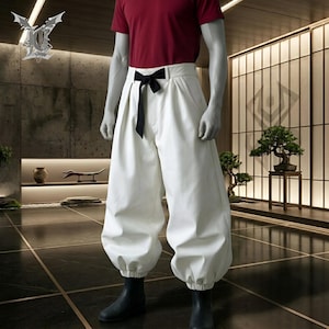 May include: A mannequin wearing a red t-shirt and white pants with a black bow belt. The pants have a unique, voluminous design, gathered at the ankles. Black boots complete the outfit. The background features a modern interior with a bonsai tree.