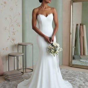 Elegant minimalist strapless mermaid wedding dress in satin fabric with delicate lace neckline, fitted bridal gown with modern boho style and long train.