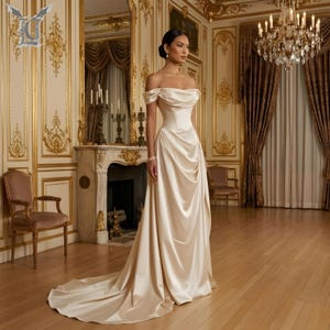 Side view of ivory satin wedding gown with soft draping, fitted waist, and romantic off shoulder sleeves