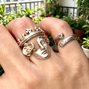 Pode incluir: Uma caneca de cerâmica branca com uma alça preta e o texto "But First, Coffee" em preto, com uma fonte manuscrita. A caneca está sobre uma superfície branca.