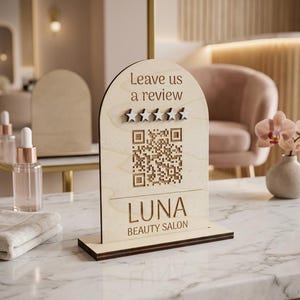 Peut inclure: Un panneau en bois clair en forme d'arche avec le texte Leave us a review, cinq étoiles en relief, un code QR et le texte LUNA BEAUTY SALON. Le panneau est fixé sur une base rectangulaire et présente un grain de bois naturel gravé.