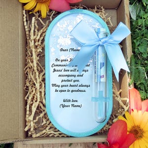 Könnte beinhalten: Geschenkbox mit hellblauem, ovalem Rahmen mit einer gedruckten Nachricht und einem transparenten Fläschchen mit blauem Band. Der Rahmen hat einen glitzernden Rand und Silberfolie. Die Box ist mit braunen Papierschnitzeln gefüllt.