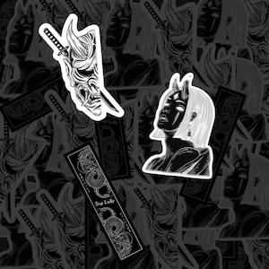 May include: A collection of black and white stickers featuring a Hannya mask pierced by a katana, a portrait of a person with horns and a bob haircut, and a rectangular bookmark-style sticker with a dragon illustration and the text Stay Lucky.