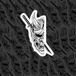May include: A die-cut sticker featuring a black and white line art illustration of a half-face Hannya mask combined with a katana sword. The design shows the sharp, horned features of the mask and the blade of the sword against a white border.