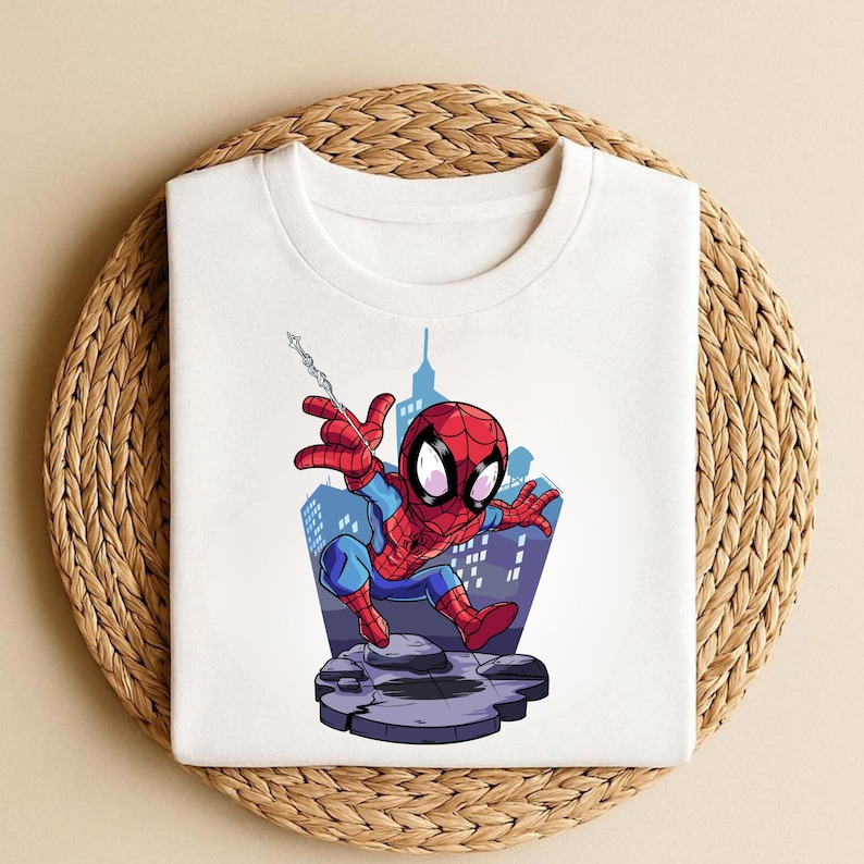 K&ouml;nnte beinhalten: Wei&szlig;es T-Shirt mit einem Cartoon-Design von Spider-Man. Die Illustration zeigt den Superhelden in seinem rot-blauen Kost&uuml;m, mit einem Stadtlandschaftshintergrund. Die Grafik ist mittig auf dem T-Shirt platziert.
