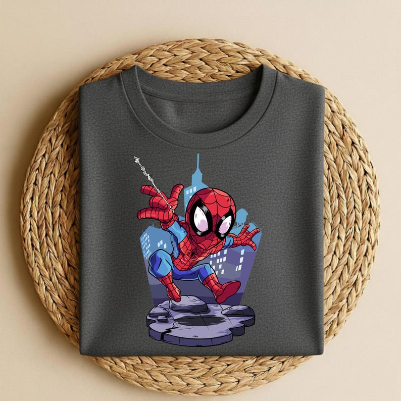 K&ouml;nnte beinhalten: Dunkelgraues T-Shirt mit einem Spider-Man-Cartoon-Motiv. Der Superheld ist in seinem klassischen rot-blauen Anzug vor einer Stadtkulisse dargestellt. Das Design ist auf einem Rundhals-T-Shirt gedruckt, ideal f&uuml;r Freizeitkleidung.