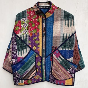 Puede incluir: Chaqueta patchwork con cuello mandarín y dos bolsillos delanteros. La chaqueta presenta una variedad de parches de tela coloridos en tonos de azul, verde, rojo, morado y amarillo. La chaqueta está acolchada y tiene un ribete azul oscuro.