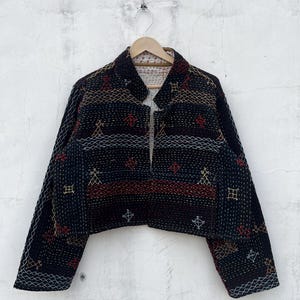 以下が含まれることがあります： 赤、黄、白の幾何学模様の複雑なカンタ刺繍が施された黒のクロップドジャケット。長袖、マンダリンカラー、フロントオープンデザインで、生地全体にキルティングのような質感が特徴です。