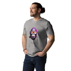 Könnte beinhalten: Ein graues T-Shirt mit einer farbenfrohen Grafik eines Affen mit Sonnenbrille. Das Gesicht des Affen ist in leuchtenden Pink-, Lila- und Orangetönen dargestellt. Der Text "MASQUERADE" ist darunter gedruckt. Das Shirt ist aus weichem Material.
