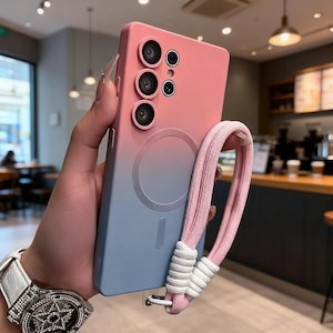 Könnte beinhalten: Eine pink-blaue Handyhülle mit Farbverlauf und mehreren Kameralinsen. Die Hülle hat einen passenden pinkfarbenen Riemen mit weißen Akzenten. Die Handyhülle wird von einer Person gehalten.