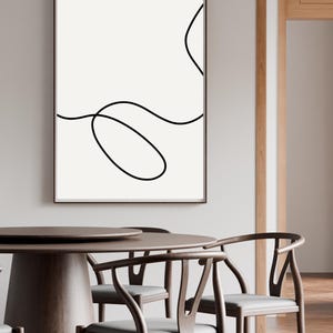 May include: A framed abstract art print with a minimalist design. The artwork features a black continuous line on a cream background. The print is displayed above a wooden dining table with matching chairs.