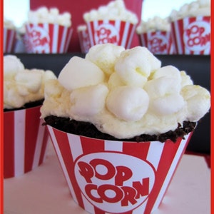 May include: Chocolate cupcakes decorated with white frosting and popcorn, topped with red and white striped cupcake liners that say "Pop Corn".
