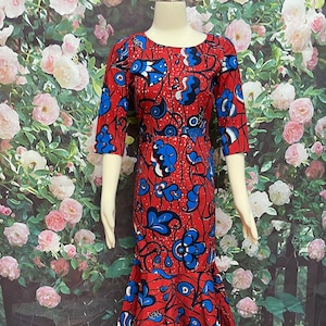 May include: A red, knee-length dress with a vibrant blue and white floral pattern. The dress features three-quarter sleeves and a mermaid-style skirt. The dress is displayed on a mannequin.