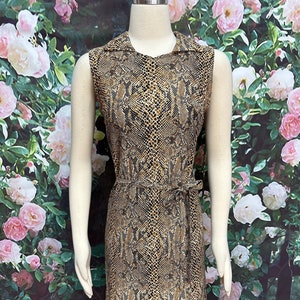 May include: A sleeveless dress with a snakeskin print in shades of brown and black. The dress has a collar and a belt.