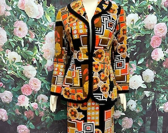 May include: A vintage 1970s style skirt suit in a bold geometric print with orange, brown, and black colors. The jacket has a black velvet trim and a single button closure. The skirt is a-line and falls to the knees.