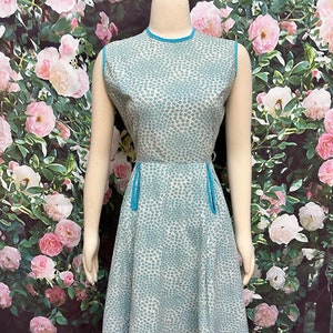 May include: A sleeveless dress with a white background and a blue floral pattern. The dress has a round neckline and a blue trim around the neckline and armholes. The dress has a fitted bodice and a full skirt.