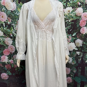 May include: A white two-piece sleepwear set consisting of a sleeveless nightgown and a matching long-sleeved robe. The nightgown features a V-neckline with lace trim and a tie-front detail. The robe has lace-trimmed cuffs and an open front design.