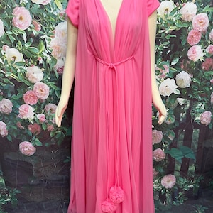 May include: A floor-length, bright pink gown featuring a deep V-neckline, short sleeves, and a sheer, flowing overlay. The garment includes a thin, matching pink tie at the waist that secures with two decorative fabric flower accents at the ends.